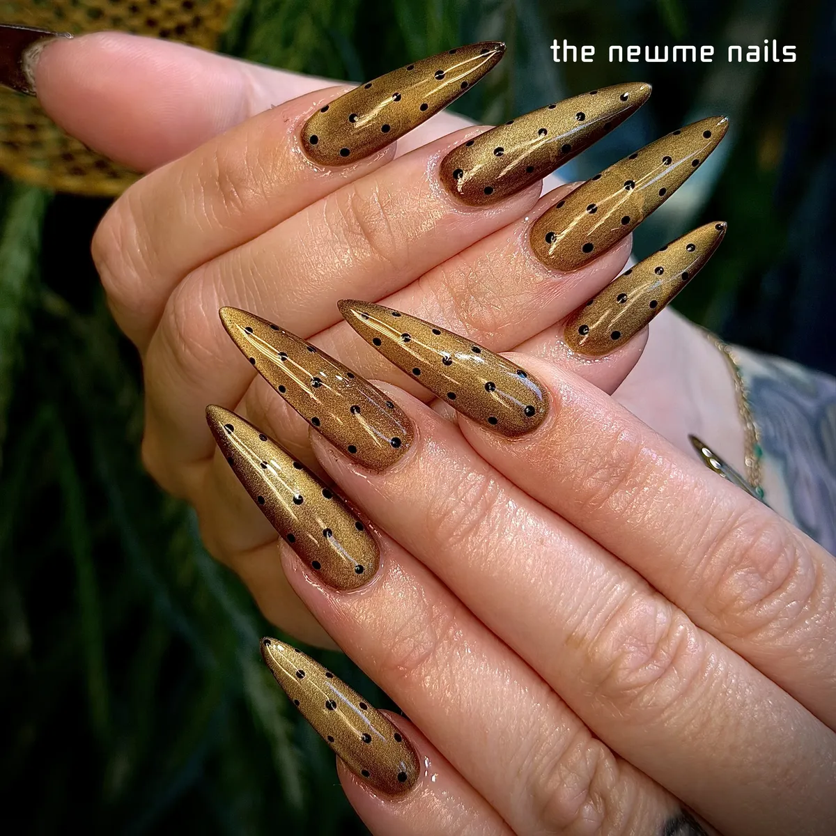 Long stilettos in shimmering gold cat-eye polish dotted with small black spots.