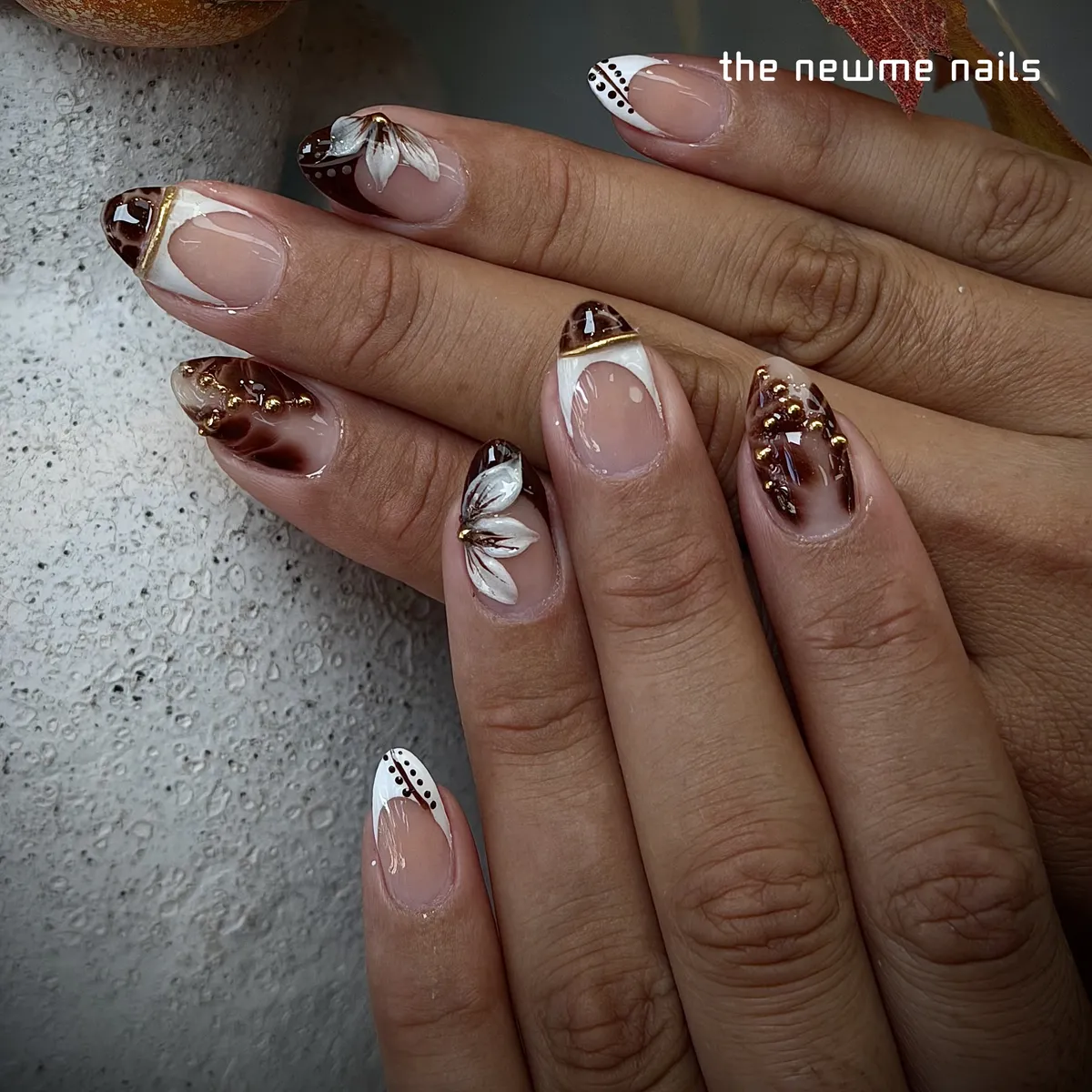 Short almond nails in sheer nude with white french tips, dark brown tortoiseshell, painted white petals, gold studs and fine gold lines.