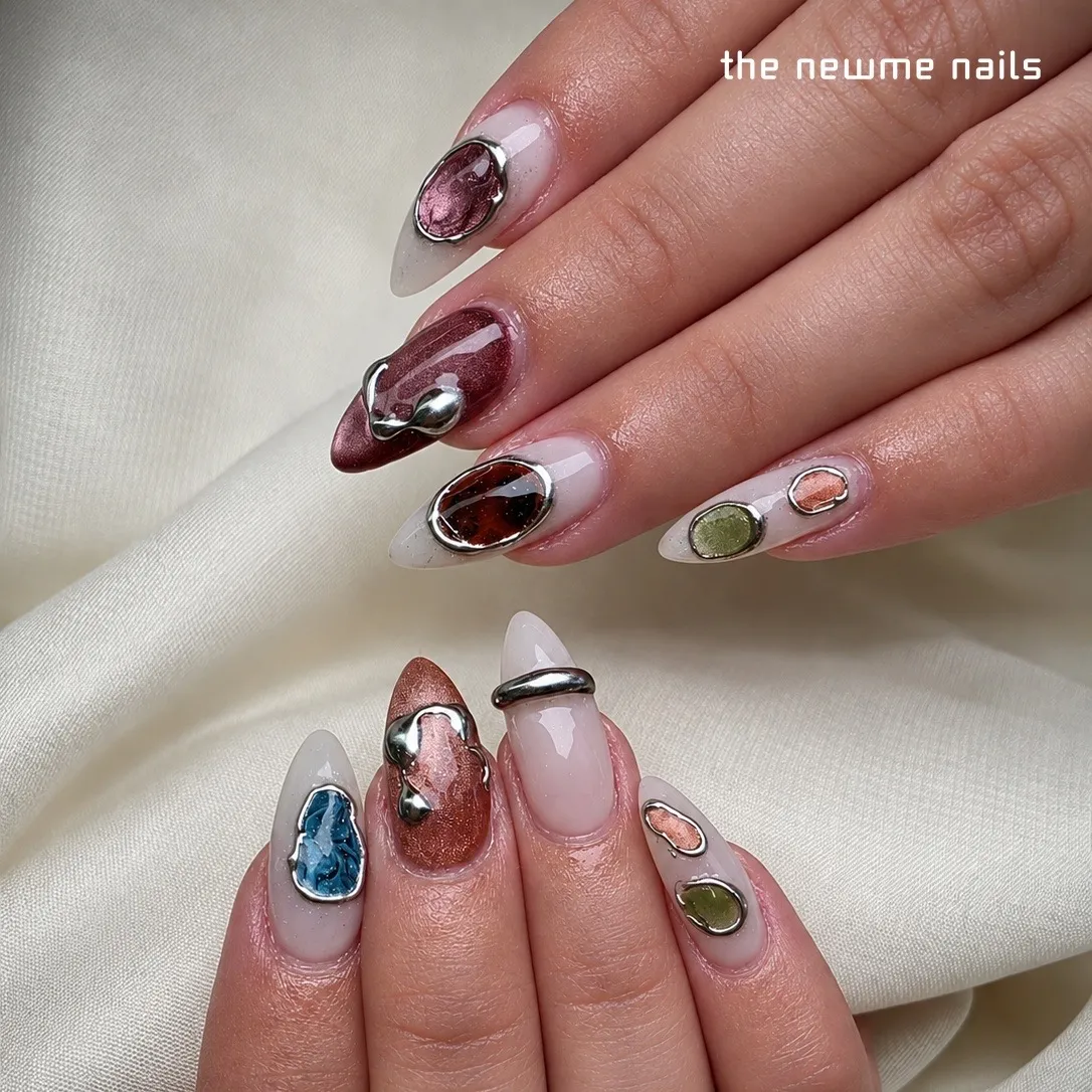 Almond nails on a milky white base set with framed stones in burgundy, tortoiseshell, blue, sage and peach, with raised liquid-silver accents.